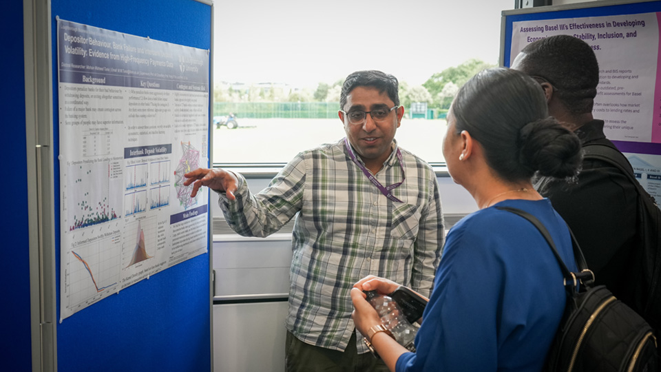 Person presenting a research poster with graphs and charts to three others, with
